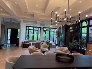 A spacious living area with a modern sofa set, a dining table, and a large TV screen.