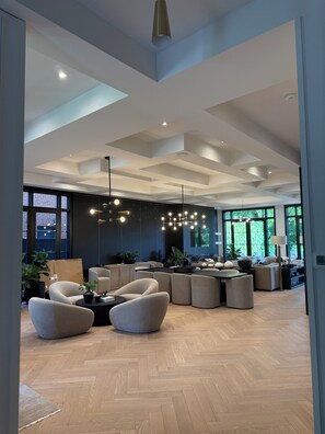 A spacious living area with a high ceiling, modern furniture, and large windows.