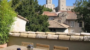 Une terrasse avec une table et des chaises, d’où l’on peut admirer un bâtiment historique doté d’une tour et d’une structure évoquant un château.