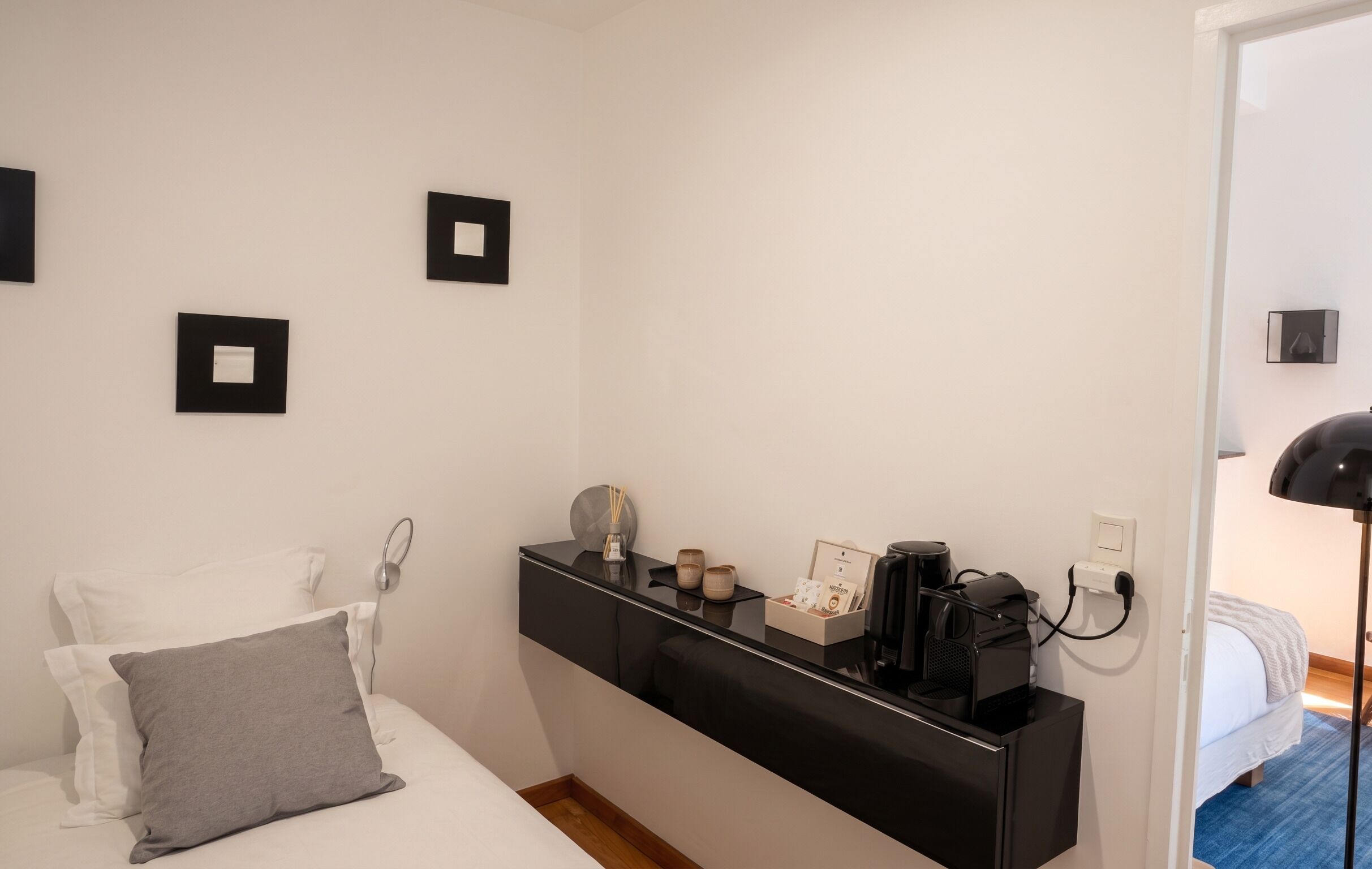Una habitación de hotel moderna con cama, mesita de noche y un pequeño escritorio con cafetera y lámpara.