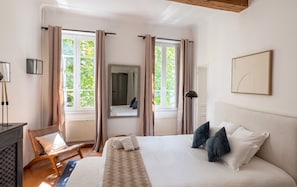 A bedroom with a bed, a chair, a desk, and a window with curtains.