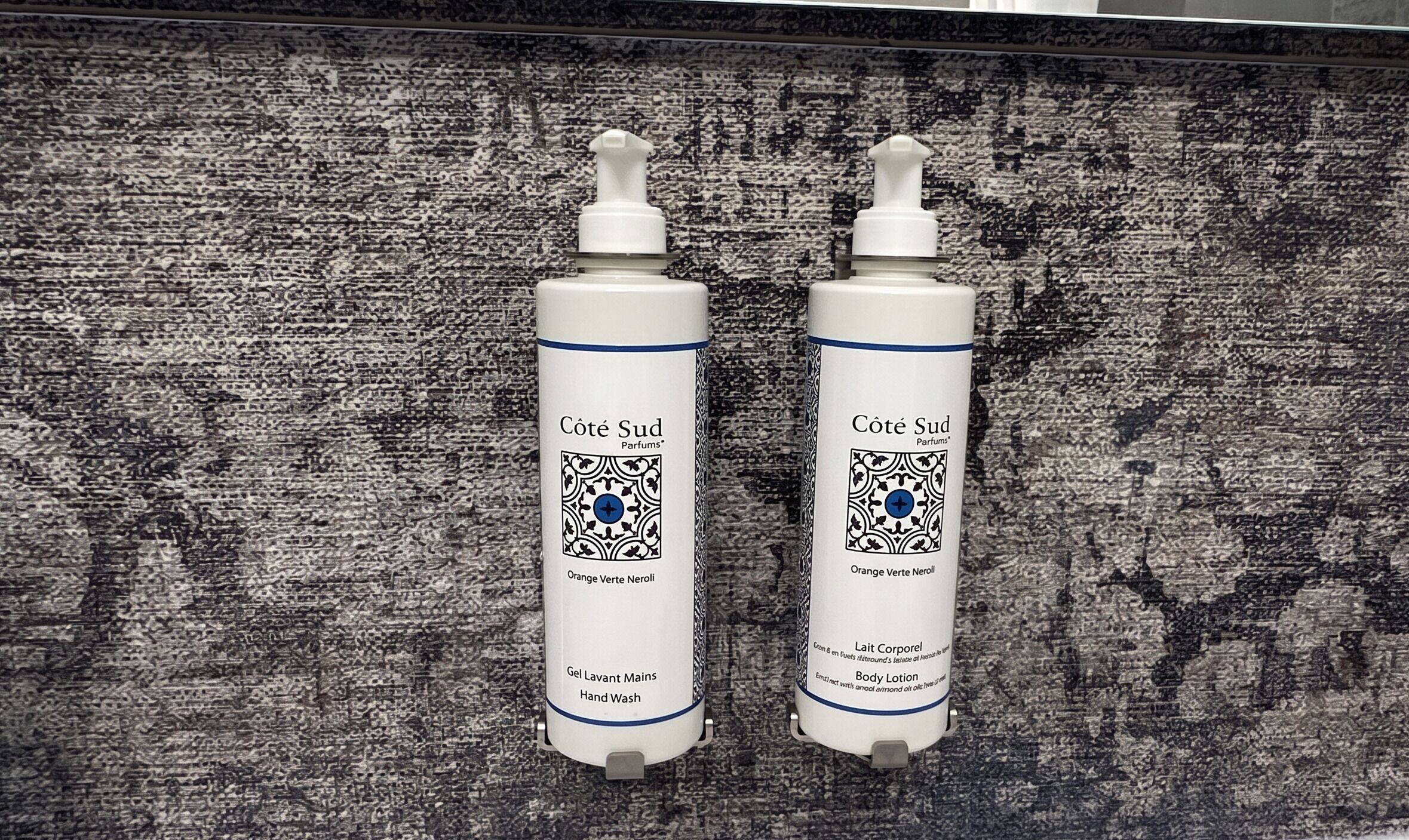 Two bottles of Côte Sud Parfums body lotion on a textured surface.