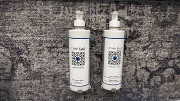 Two bottles of Côte Sud Parfums body lotion on a textured surface.