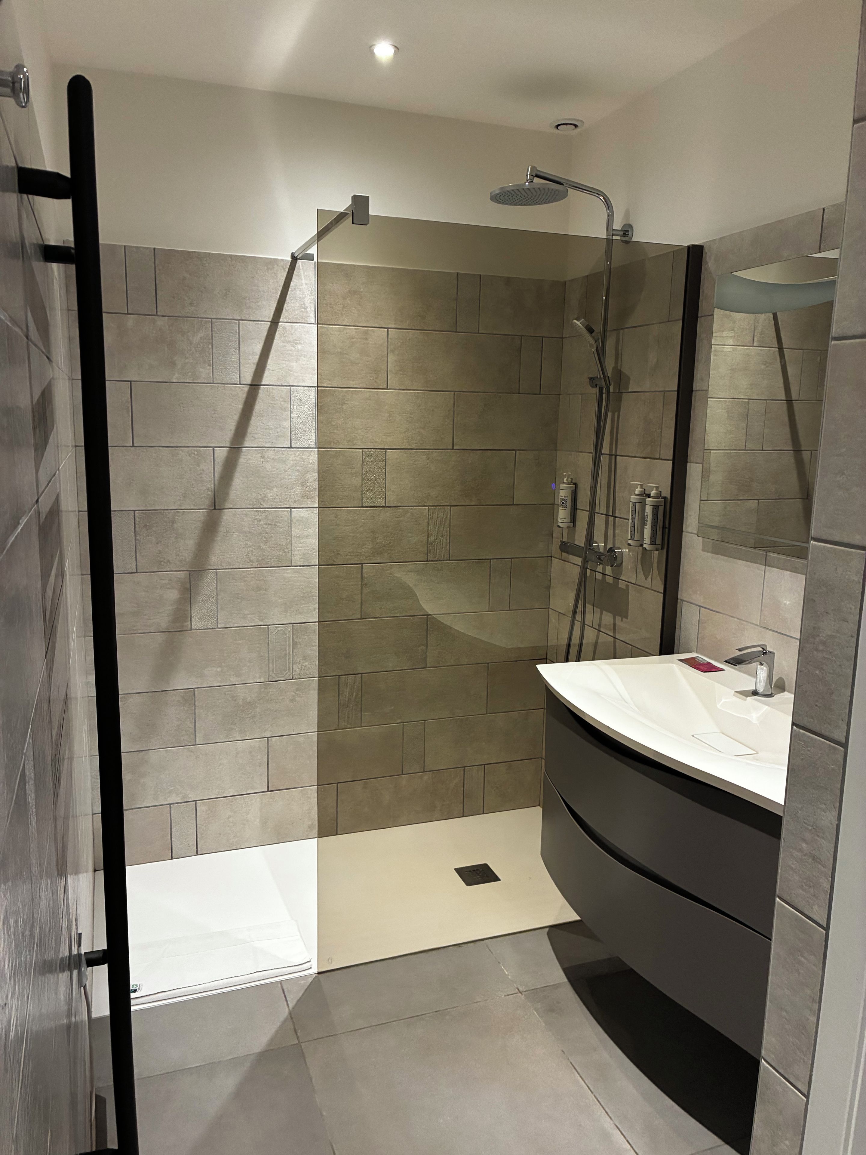 A modern bathroom with a walk-in shower, a curved vanity, and a large mirror.