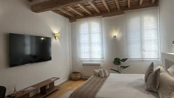 A bedroom with a large bed, a flat-screen TV mounted on the wall, and two windows with light fixtures.