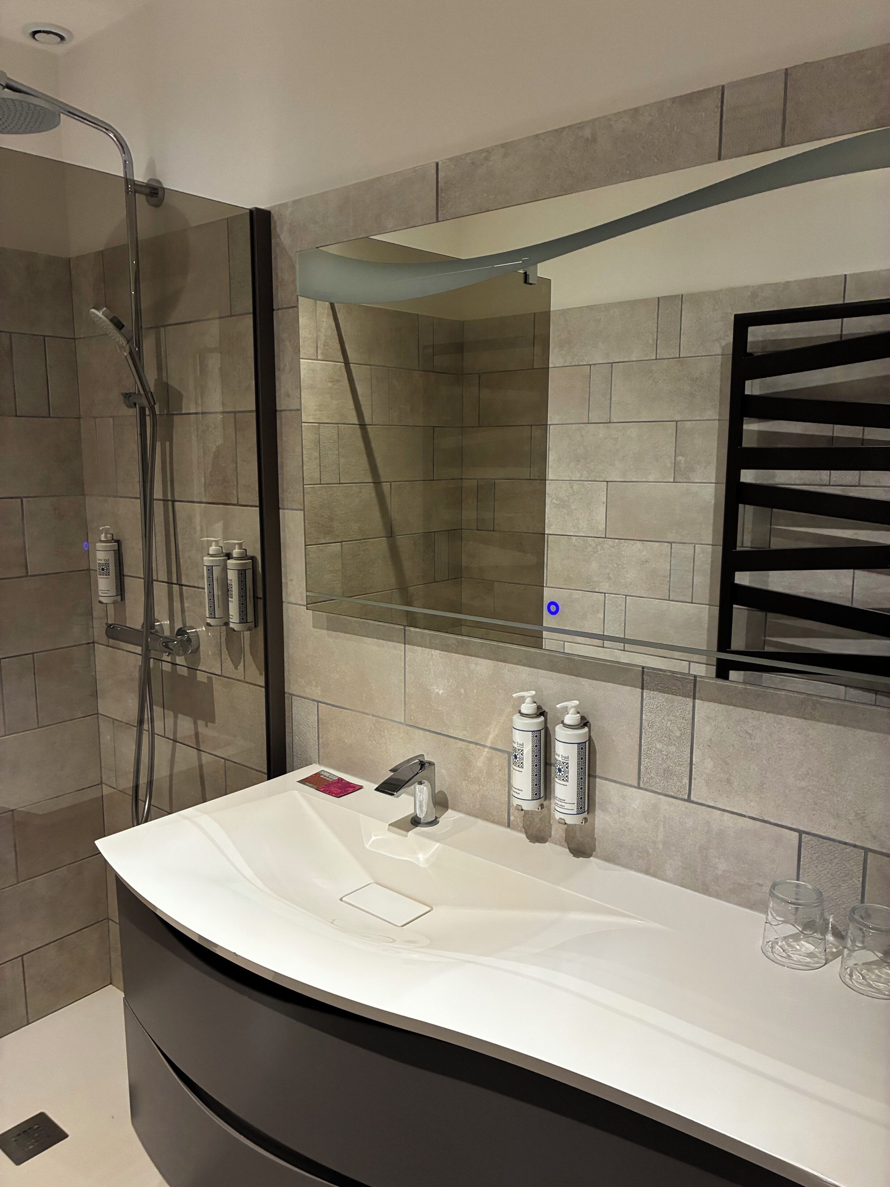 A modern bathroom with a curved white sink, a glass shower enclosure, and a mirror with a black frame.