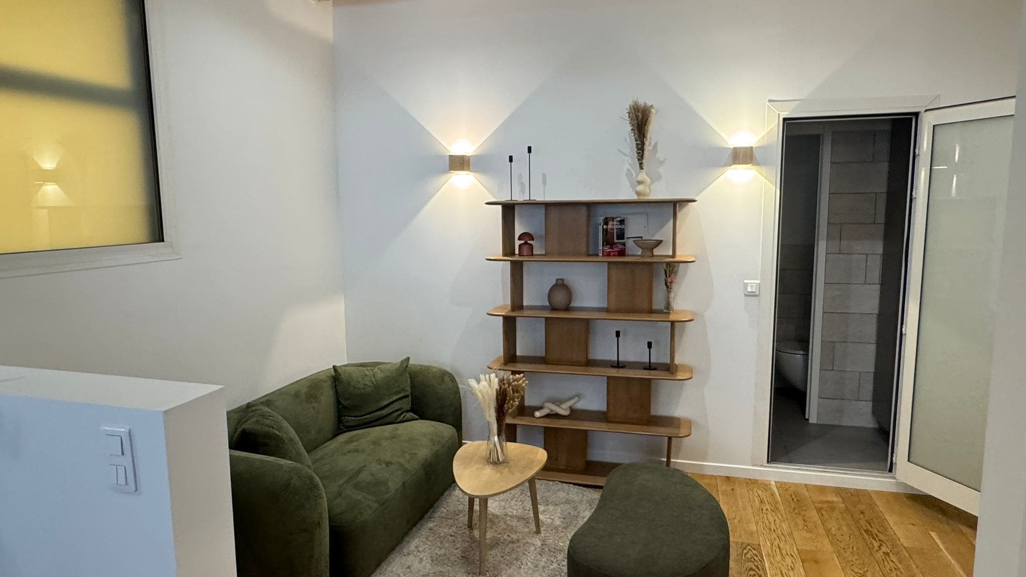 Een knus woongedeelte met een bank, een klein rond tafeltje en een houten wandplank.