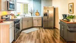 Cozinha com piso de madeira, eletrodomésticos de aço inoxidável e armários em tons claros.