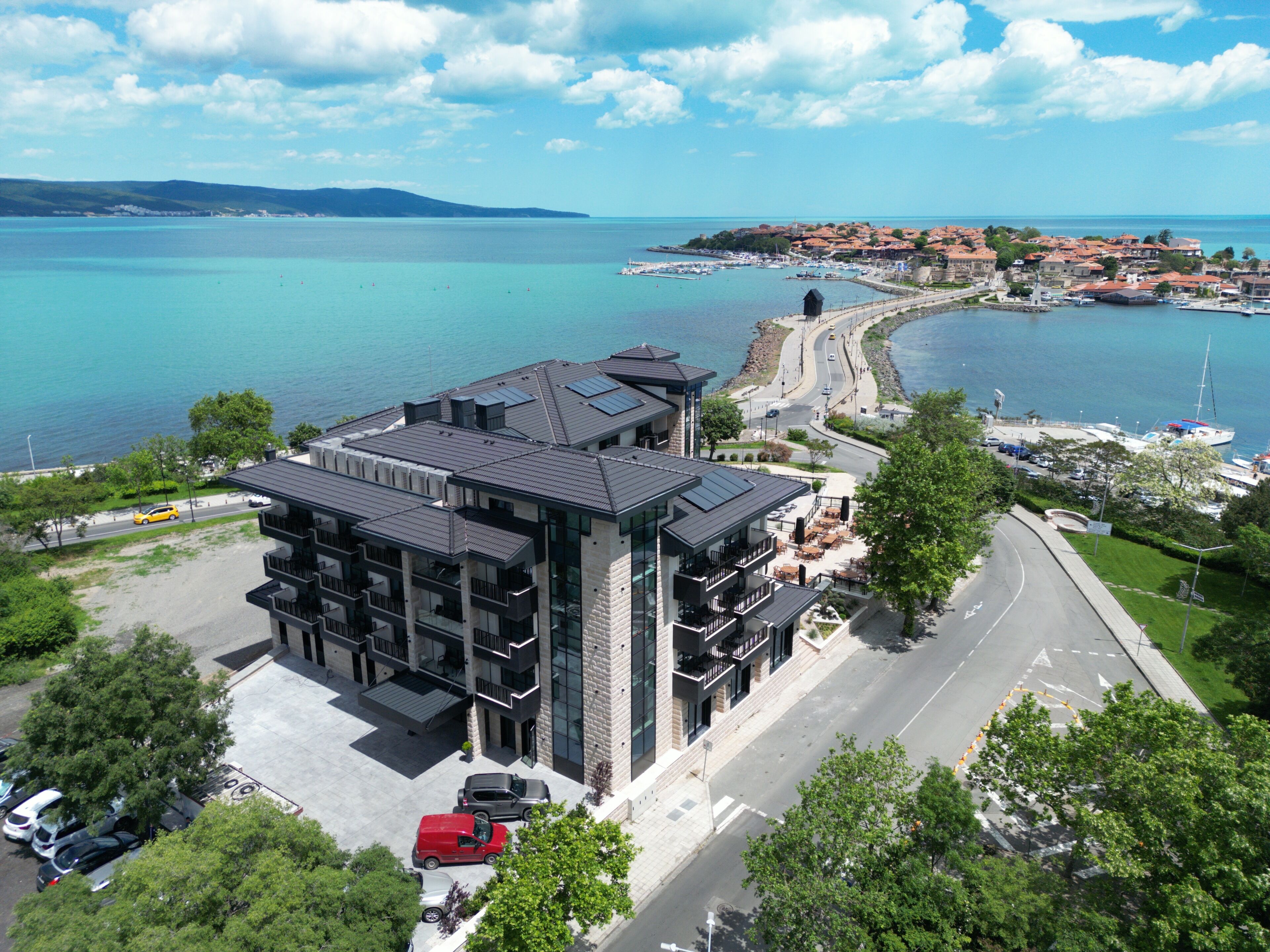 Un hotel moderno con estacionamiento, una carretera y vistas al mar y un pueblo pequeño.