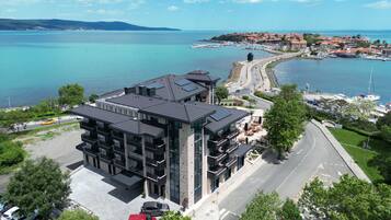 Un hotel moderno con estacionamiento, una carretera y vistas al mar y un pueblo pequeño.
