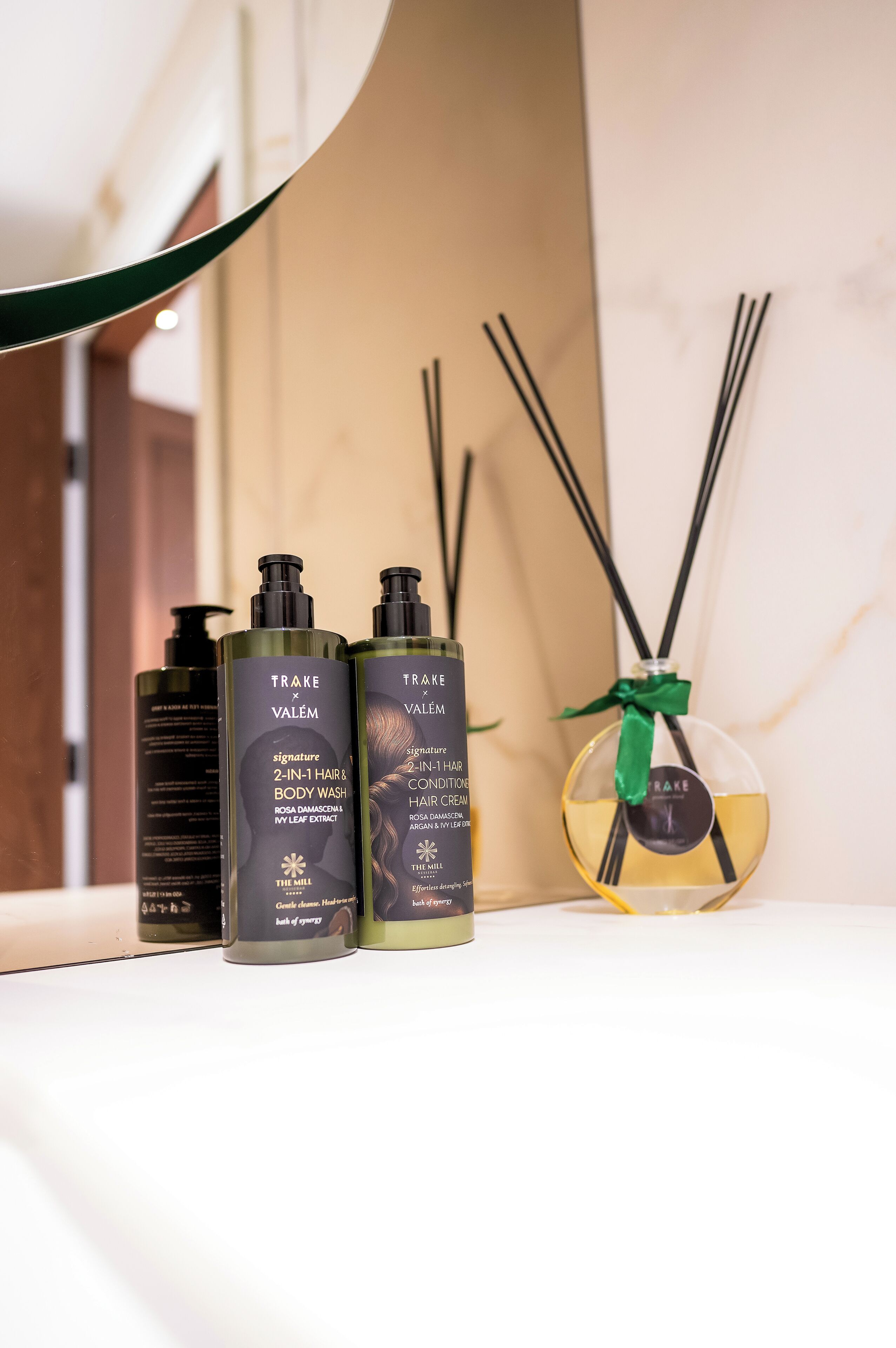 A bathroom with three bottles of Trake Valem hair and body wash, a reed diffuser, and a mirror.