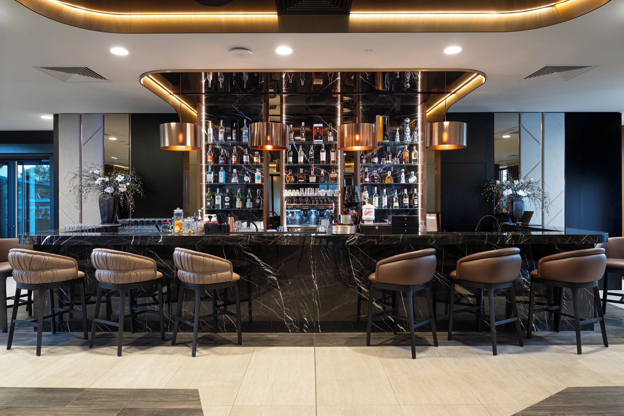 Zona de bar con mostrador de mármol, varias botellas de licor y taburetes de cuero.