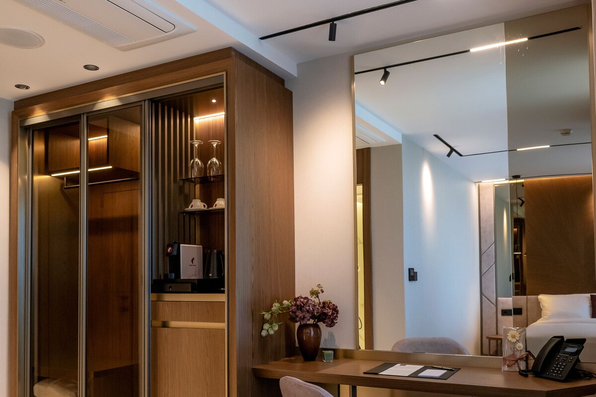 A modern hotel room with a desk, chair, wardrobe, and a large mirror.