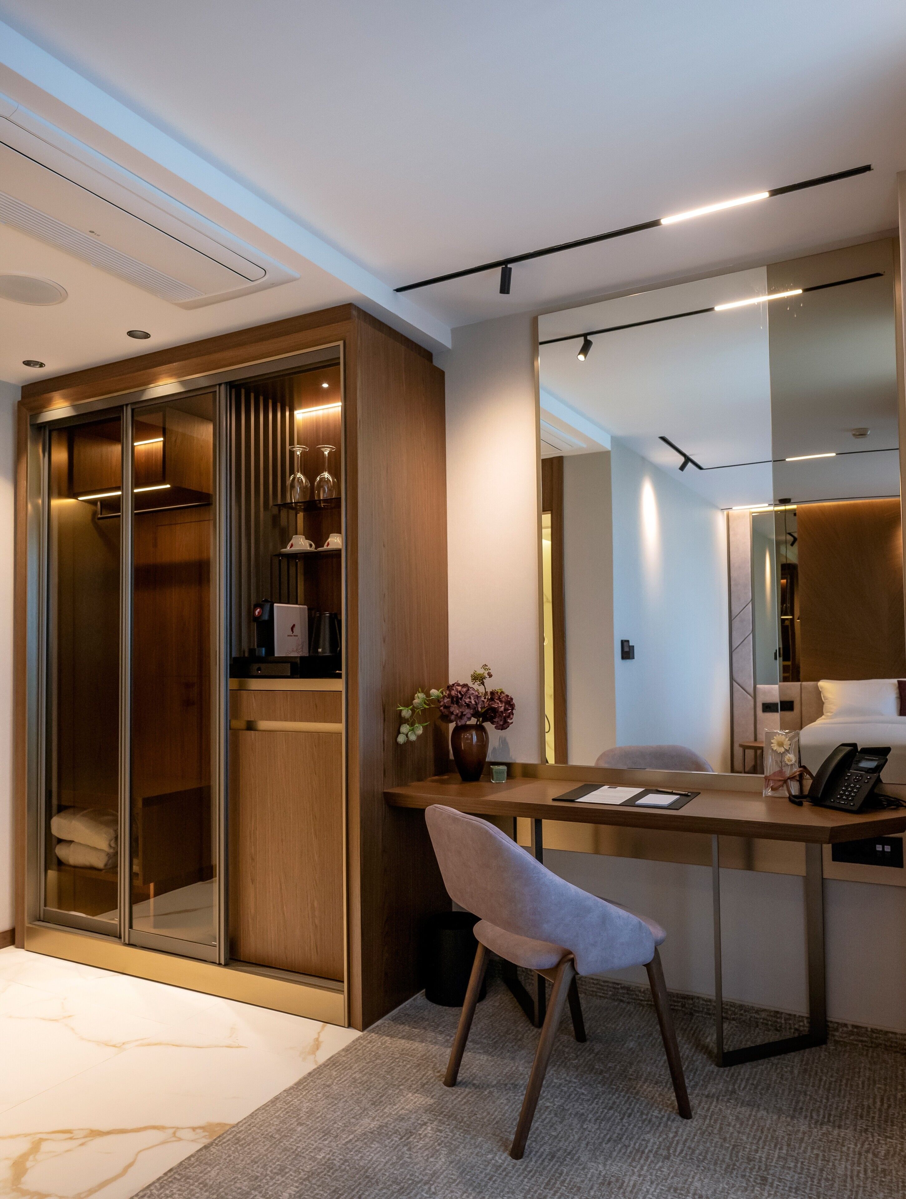 Una habitación de hotel moderna con escritorio, silla, armario y un espejo grande.