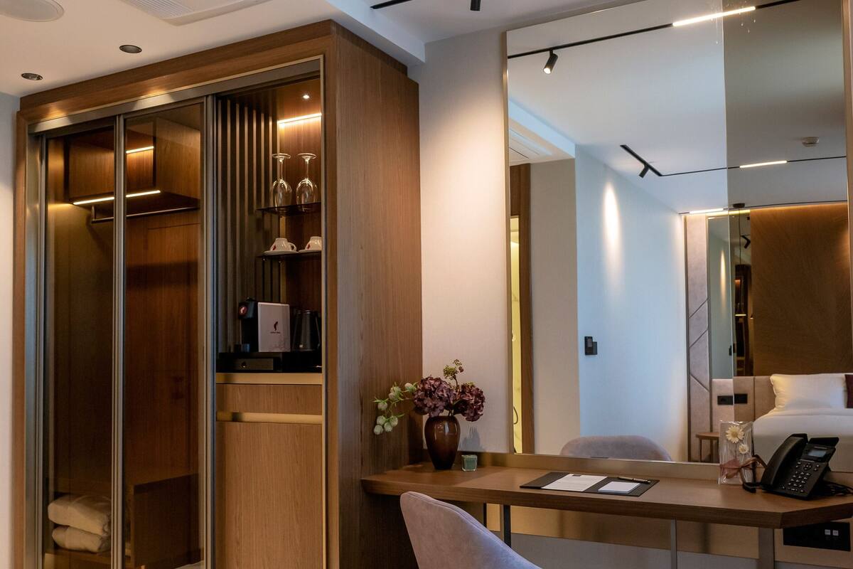 Una habitación de hotel moderna con escritorio, silla, armario y un espejo grande.
