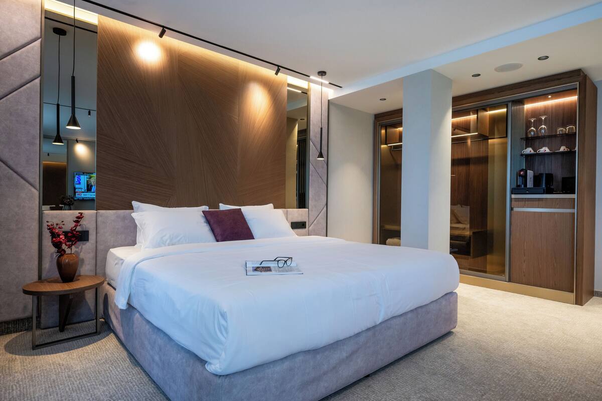 Habitación de hotel moderna con una cama grande, una mesita de noche con un jarrón, un armario y un escritorio con una computadora.