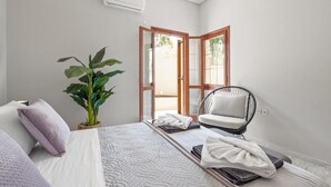 Ein Schlafzimmer mit einem Bett, einem Sessel, einer Topfpflanze und einer Tür zu einem Außenbereich.