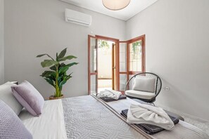 A bedroom with a bed, a chair, a potted plant, and a door leading to an outdoor area. - STR Sodi The View (Chania)