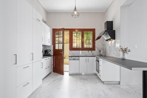 A modern kitchen with white cabinetry, a built-in oven, and a window with a view of greenery. - STR Sodi The View (Chania)