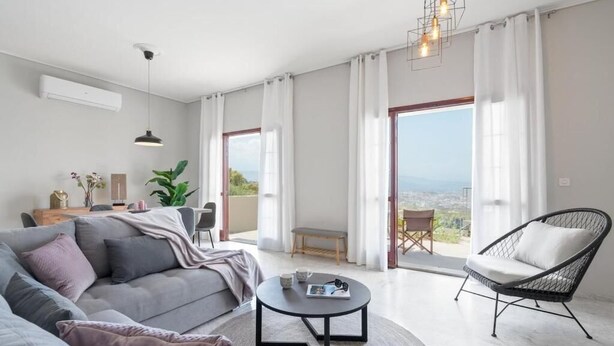 Ein modernes Wohnzimmer mit einer Couch, einem runden Couchtisch, einem Korbstuhl und Blick durch große Fenster.