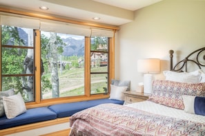A bedroom with a large window, a bed, a bedside table with a lamp, and a view of a mountainous landscape. - Aspen Ridge 25 3 Bedroom Townhouse (Telluride)