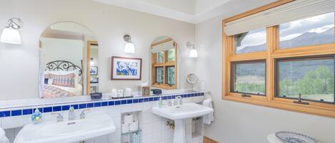 A bathroom with two sinks, a mirror, a window with a view, and a blue patterned rug.