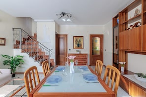 A dining area with a glass-top table, chairs, a staircase, and a wooden cabinet with decorative items. - VILLA CATERINA A FEW STEPS FROM THE SEA: PET FRIENDLY, BBQ, TERRACE & RELAX (San Bartolomeo al Mare)