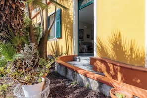 A yellow building with a staircase leading to an open door, surrounded by potted plants and a palm tree. - VILLA CATERINA A FEW STEPS FROM THE SEA: PET FRIENDLY, BBQ, TERRACE & RELAX (San Bartolomeo al Mare)