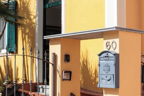 Uma caixa de correio com o número 60, uma porta e uma pequena placa numa parede de edifício.