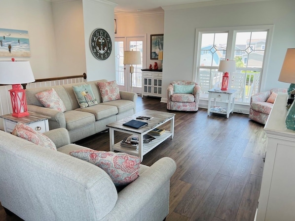 A living room with a sofa, armchair, coffee table, and a clock on the wall. - Salty Forever / 105 Shell Drive 4 Bedroom Home (Supply)