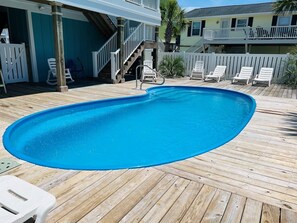 Una terraza de madera con piscina, sillas de descanso blancas y una escalera que lleva a un edificio.