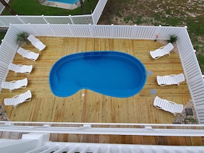 Ein rechteckiger Pool mit Holzterrasse und weißen Liegestühlen darum herum.