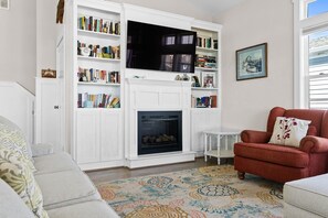Ein Wohnzimmer mit Kamin, Bücherregalen, einem roten Sessel und einem gemusterten Teppich.