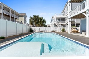 Une piscine rectangulaire dont le bord est recouvert de carrelage, entourée d’une terrasse en bois.