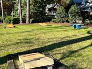 A well-maintained grassy area with wooden structures, likely for outdoor activities, surrounded by trees and a residential building in the background. - Golden Memories / 91 Genoes Point Rd 2 Bedroom Home (Supply)