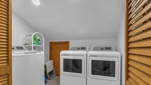 A laundry room with three stacked washers and dryers, a drying rack, and a shelf with cleaning supplies. - Sea You Reel Soon / 1207 Ocean Blvd. West 6 Bedroom Home (Supply)