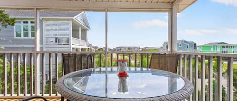 Un espace extérieur abrité avec une table et des chaises en verre, un objet rouge sur la table et, en arrière-plan, une vue sur des maisons.