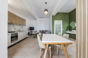 Une cuisine moderne avec des appareils électroménagers blancs, un coin repas avec une table et des chaises en bois, et un mur d’accent vert.