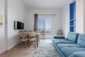 Ein modernes Wohnzimmer mit Flachbildfernseher, einer Couch, einem Esstisch mit Stühlen und einem Balkon mit Meerblick.