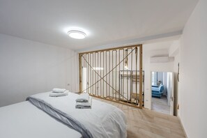 Ein Schlafzimmer mit einem Bett, einem Holzschrank und Blick auf ein blaues Sofa im angrenzenden Raum.