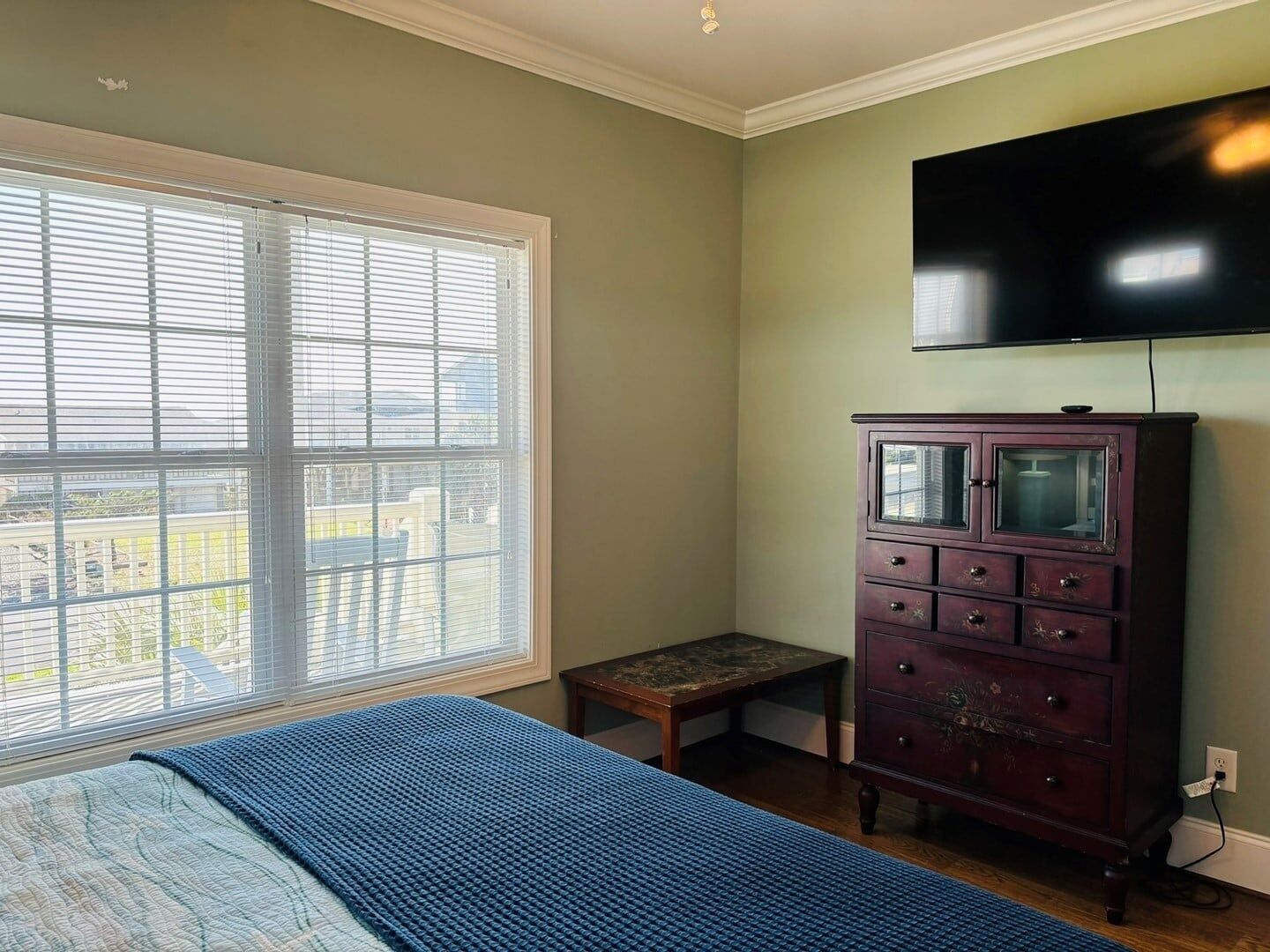 A bedroom with a bed, a dresser, a television, and a window with blinds.