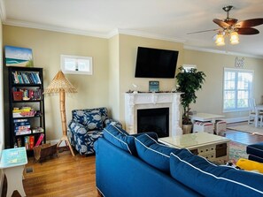 Ein Wohnzimmer mit Sofa, Bücherregal, Kamin, Fernseher und Deckenventilator.