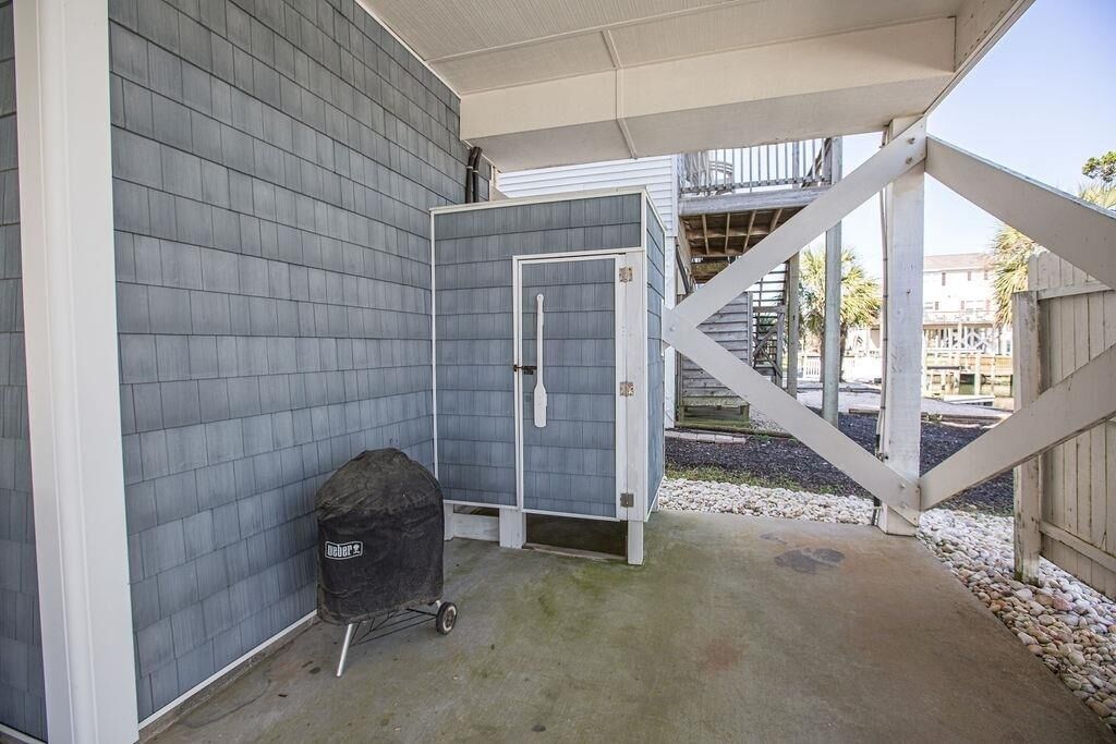 A covered outdoor area with a grill, a door, and a staircase leading to a balcony.