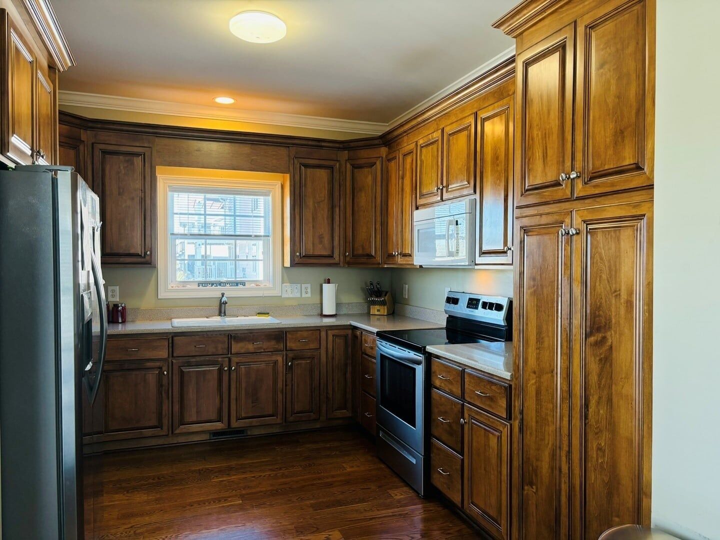 A kitchen with wooden cabinets, a stainless steel refrigerator, a microwave, an oven, and a sink.