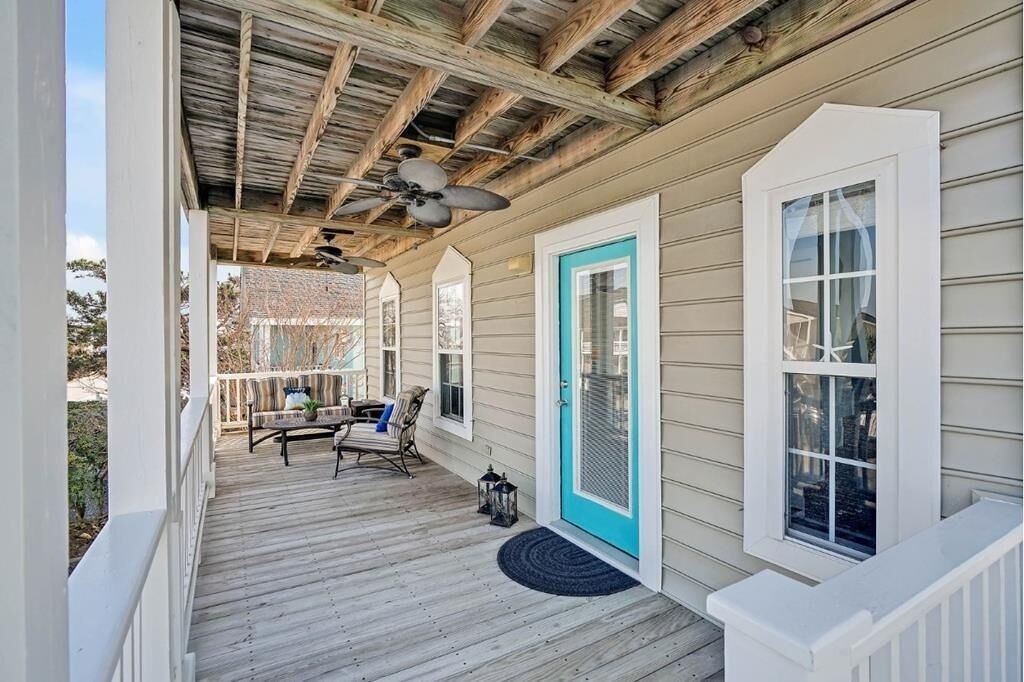 A covered porch with a ceiling fan, a door with a blue frame, and a window with a white frame.