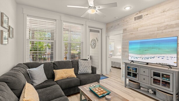 A living room with a grey sectional sofa, a wooden coffee table, a flat-screen TV, and a ceiling fan. - 30a Getaway 3 Bedroom Condo (Santa Rosa Beach)