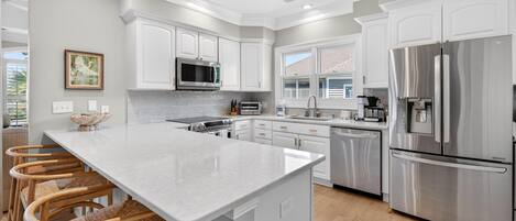 Una cocina moderna con armarios blancos, electrodomésticos de acero inoxidable y una isla central con taburetes de bar.