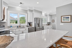 A modern kitchen with white cabinetry, stainless steel appliances, a large island, and a view of the outdoors.