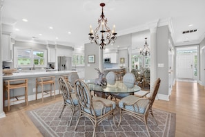A spacious kitchen with white cabinetry, a central island, and a dining area with wicker chairs and a glass table.