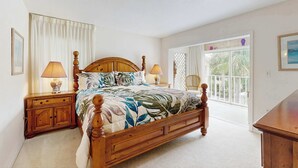 A bedroom with a wooden bed, two bedside tables with lamps, a window with curtains, and a view of greenery outside. - Venice Condo, Pool, Balcony & Beaches Nearby! (Venice)